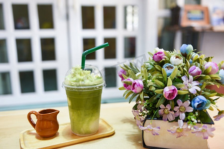 拿牛奶摄影照片_绿茶冰沙/抹茶绿茶与牛奶的塑料玻璃上的桌子在咖啡馆