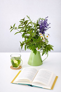 生态和有机概念—一杯绿色草本茶，书和鲜花放在桌子上。在桌子上壶中提供草药茶、书籍和鲜花