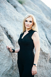 在灰色瓦砾中的花岗岩采石场的背景上，穿着黑色裤装的金发女孩有着蓝色的眼睛