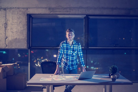 年轻男性工程师在建筑工地检查文件和业务工作流程使用膝上型计算机在晚上新的启动办公室
