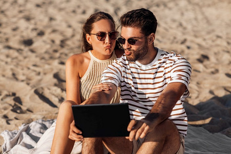 休闲与人的概念-在夏日海滩与平板电脑幸福的情侣。夏日海滩上，一对幸福的夫妇带着平板电脑
