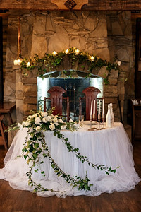 餐厅宴会厅的新婚夫妇主席团用蜡烛和绿色植物装饰，紫藤从天花板上垂下来