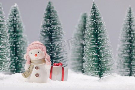 在雪地圣诞卡设计的森林里有礼物的小可爱玩具雪人。森林里有礼物的雪人