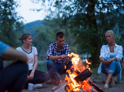 一群快乐的年轻朋友在河边篝火旁放松，享受夏日的夜晚