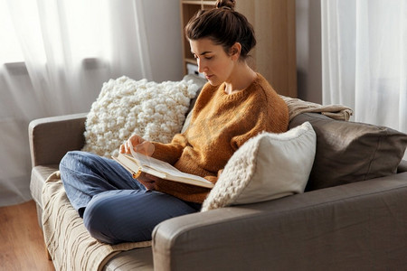 人和休闲概念—粉红色衬衫的年轻妇女坐在沙发和读书在家。年轻女子在家读书