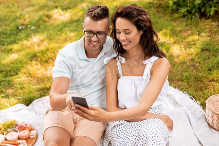 与人连接摄影照片_休闲与人的概念快乐夫妇带着智能手机在夏季公园野餐。带着智能手机在公园野餐的幸福情侣