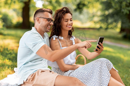 休闲与人的概念快乐夫妇带着智能手机在夏季公园野餐。带着智能手机在公园野餐的幸福情侣