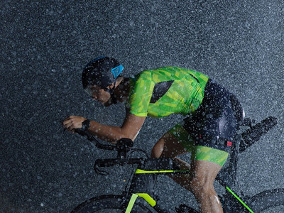 铁人三项运动员骑专业赛车自行车在晚上与恶劣的天气和下降的雨