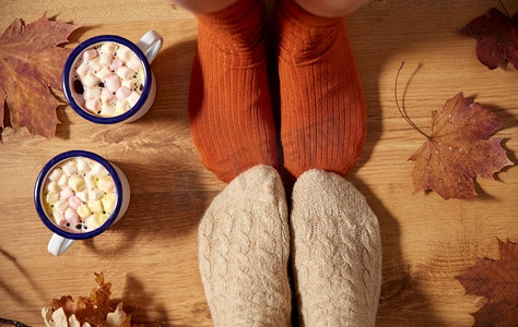 赛季摄影照片_季节和休闲概念—夫妇的咖啡杯，秋天的叶子和脚在袜子在家里。穿着袜子、咖啡和秋天的树叶