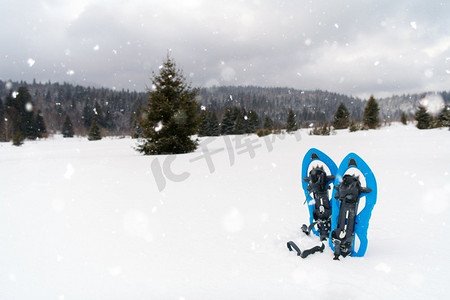 冬天徒步旅行在山的蓝色雪鞋在新鲜的显示与雪花在他们周围在下雪的冬天