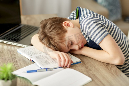 儿童、教育和学习理念-疲惫的学童睡在家里的书桌上。疲惫的男学生睡在家里的书桌上