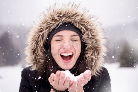 穿冬天衣服的愉快的年轻妇女，而吹雪在下雪天有雪花在她周围在美丽的冬天森林