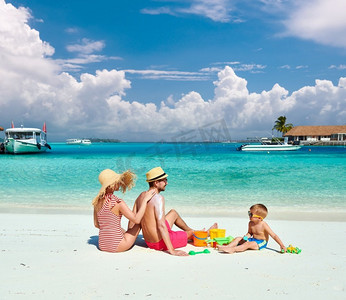 海滩上的一家人，带着三岁男孩的年轻夫妇。女性在男士S背上涂防晒霜。在马尔代夫度暑假。