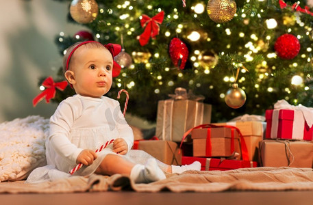 节日和童年的概念-可爱的女婴在家中圣诞树彩灯下带着礼物。圣诞树上的小女孩在家里带着礼物