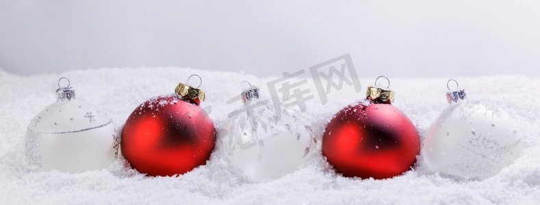 圣诞红白相间的装饰品装饰品在轻背景下的雪地上。雪中的圣诞红白相间的小玩意