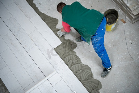 砖摄影照片_熟练工人在地板上安装陶瓷木质效果砖工人在新公寓建筑工地上制作强化地板