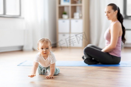 非婚子女摄影照片_家庭、运动和母性概念-快乐的微笑妈妈和小宝宝坐在家里的运动垫上。快乐的妈妈带着小宝宝在家里