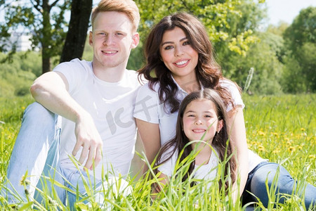 三口之家坐在春天公园的草地上很开心.人物特写婚纱写真