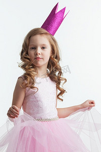 艾莎公主摄影照片_可爱的小女孩穿着粉色的万圣节公主服装，戴着孤立的皇冠，白色背景。王冠公主