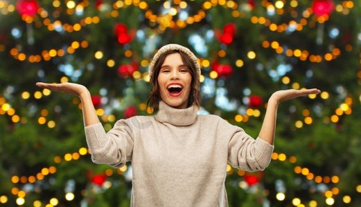 冬季假期和人概念—微笑的妇女在圣诞树灯背景快乐的女人拿着东西在圣诞树上