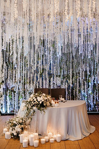 宴会厅摄影照片_餐厅宴会厅的新人主席团用蜡烛和绿色植物装饰，紫藤悬挂在天花板上，