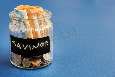 印有欧元纸币的储蓄瓶，硬币为蓝色背景。高分辨率照片。印有欧元纸币的储蓄瓶，硬币为蓝色背景。高质量照片