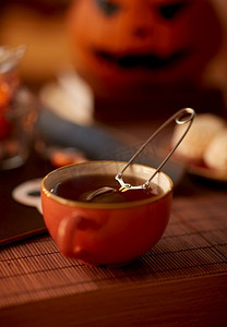 饮料，假日和休闲概念—网茶注入球在陶瓷杯在家里万圣节。在万圣节的陶瓷杯中的网眼茶注入球