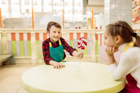 孩子们摄影照片_小男孩给女孩手工制作的棒棒糖。在糕点店的车间里，孩子们学习制作焦糖。糖果店里的节日乐趣
