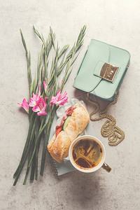 可爱的美感早餐或午餐，有咖啡和三明治，旁边有一束鲜花和一个小女人&S手袋。顶视图