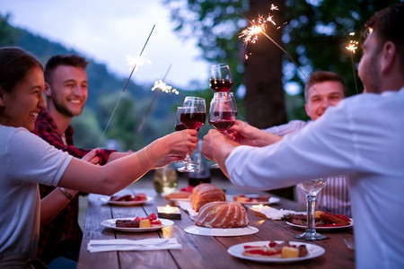 一群快乐的朋友在大自然中美丽的夏日晚上在河边户外野餐法式晚宴时