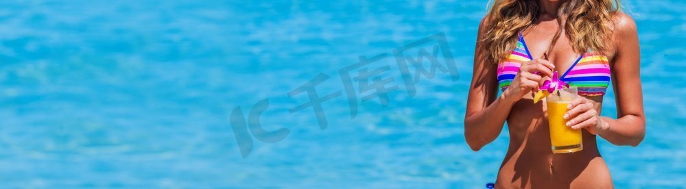 美女比基尼摄影照片_比基尼美女拿着喝橙色鸡尾酒在热带蓝色海水背景与复制空间。女人在比基尼与饮料