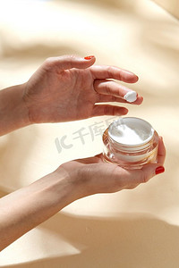 指尖的摄影照片_美容产品、化妆品和人的概念-米色背景下的女性手持保湿瓶。女性手持保湿霜瓶