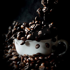 杯充满了下降热新鲜冒着热气的咖啡豆在黑色。下降的咖啡豆在白色杯子