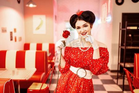 性感的别针与化妆持有红玫瑰，礼服与波尔卡点，复古风格。复古咖啡厅内部与棋盘地板