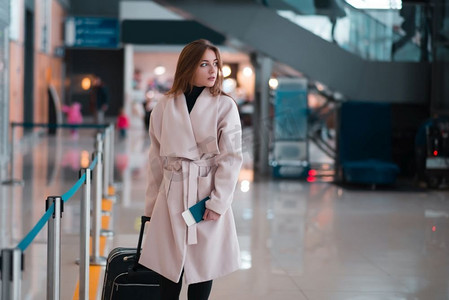 年轻的女旅行者在机场大厅拖着行李。在机场大厅散步的旅客。
