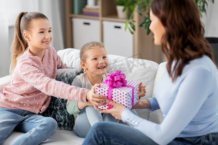 人，家庭和假期概念—两个女儿在家里给快乐的母亲送礼物。女儿给快乐的母亲送礼物