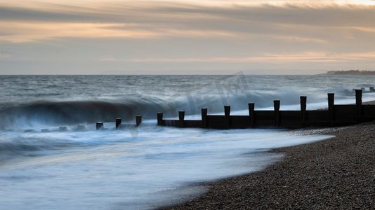 抽象海浪摄影照片_美丽的抽象长曝光景观图像，海浪在日落时撞击海滩上的丁坝