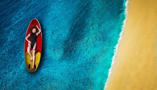在潜水衣的好的女运动员帆板运动员躺在船上，顶视图海洋和海岸在背景