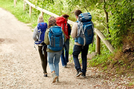 传奇大背包摄影照片_冒险，旅行，旅游，徒步旅行和人的概念—一群朋友走在树林里背包。一群背着背包徒步旅行的朋友