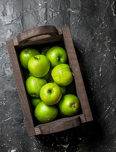 原框摄影照片_一个木箱里的青苹果。在一个黑暗的木制背景。一个木箱里的青苹果。