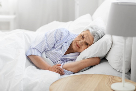 老年人和人的概念—高级妇女躺在床上在家里卧室。高级妇女躺在床上在家里卧室