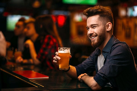 一位年轻人在一家体育酒吧的柜台前喝啤酒。一名男子在体育酒吧的吧台前喝啤酒