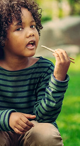 快乐的非裔美国孩子在公园里吃着快餐棒。儿童营养概念..快乐的非裔美国儿童吃零食棒。