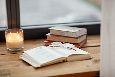 阅读，休闲和物品概念—书籍，眼镜和蜡烛在窗台上燃烧。窗台上燃烧的书、玻璃杯和蜡烛