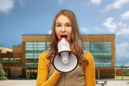 教育和人的概念—十几岁的女孩在校园背景下对着扩音器说话。十几岁的女孩说话的扩音器超过学校