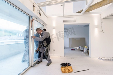 窗套摄影照片_专业木匠在一套带全景窗的新公寓里安装阳台门