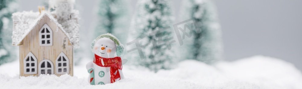 小装饰雪人附近的木屋在冷杉林下落雪。冬天的雪人和房子