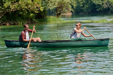一对冒险的探险家朋友正在一条被美丽的大自然环绕的野生河流中划独木舟，