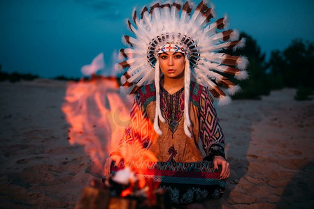 反对篝火的美国印第安女孩在晚上，女性萨满，切罗基，纳瓦霍。用野鸟羽毛制成的头饰。传统仪式