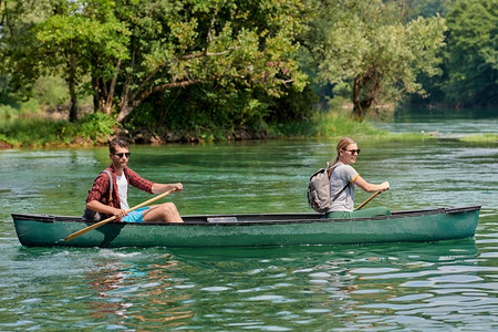 一对冒险的探险家朋友正在一条被美丽的大自然环绕的野生河流中划独木舟，